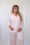 Woman wearing Goodnight Goose peach gingham women's bamboo pajama set with long-sleeve button-up top and matching pants